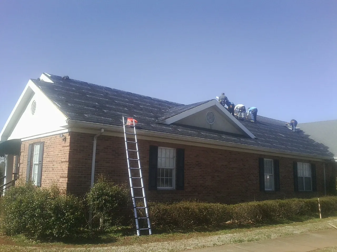 Crew tearing shingles off a brick ranch roof with a ladder set — Emergency Roof Repair work by our crew in Evansville