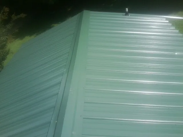 New green metal panels meeting at the ridge of a roof — Flat Roof Repair work by our crew in Evansville