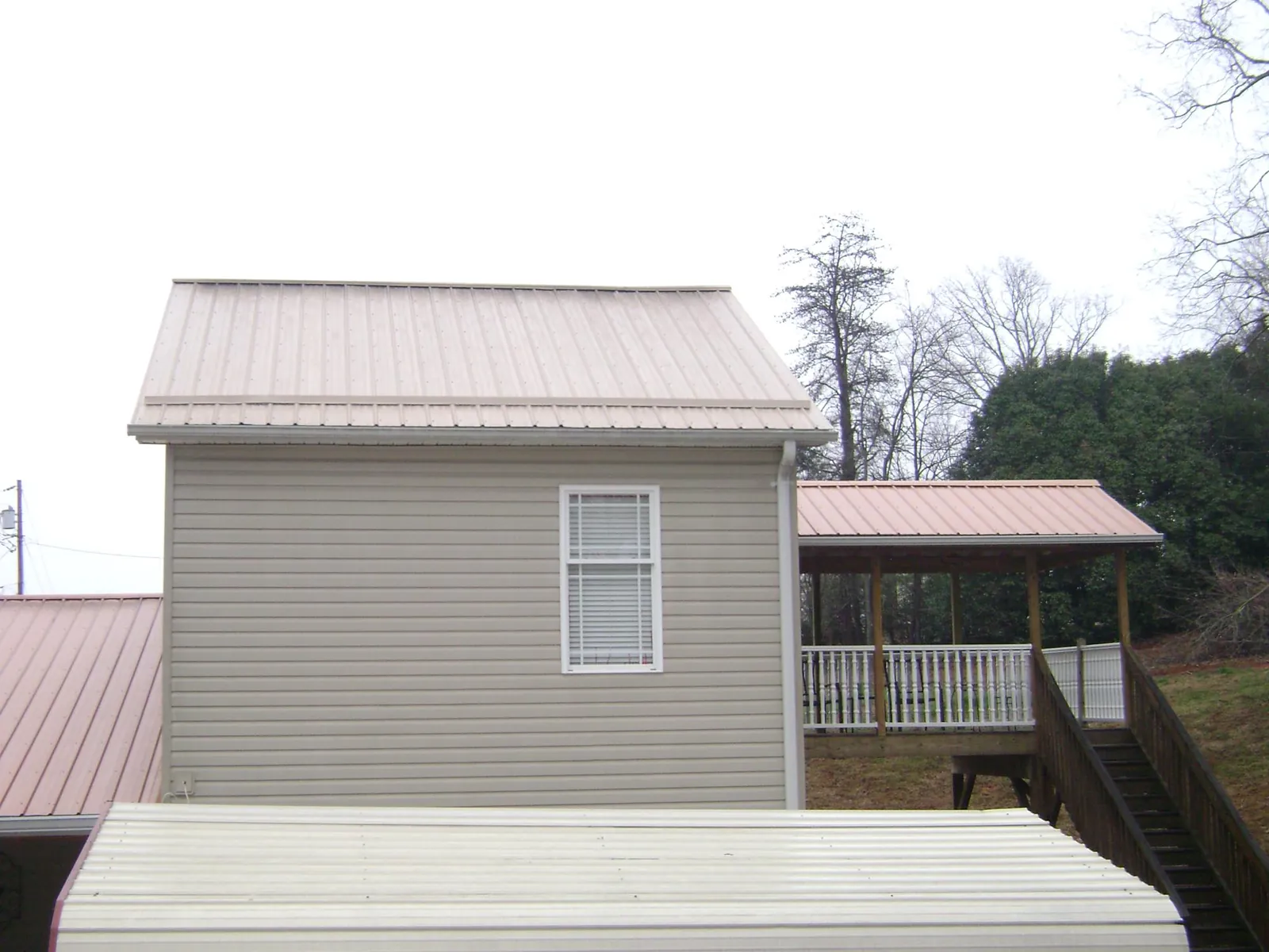Tan metal roofs on a two story addition and attached porch, from a Roof Replacement job in Evansville